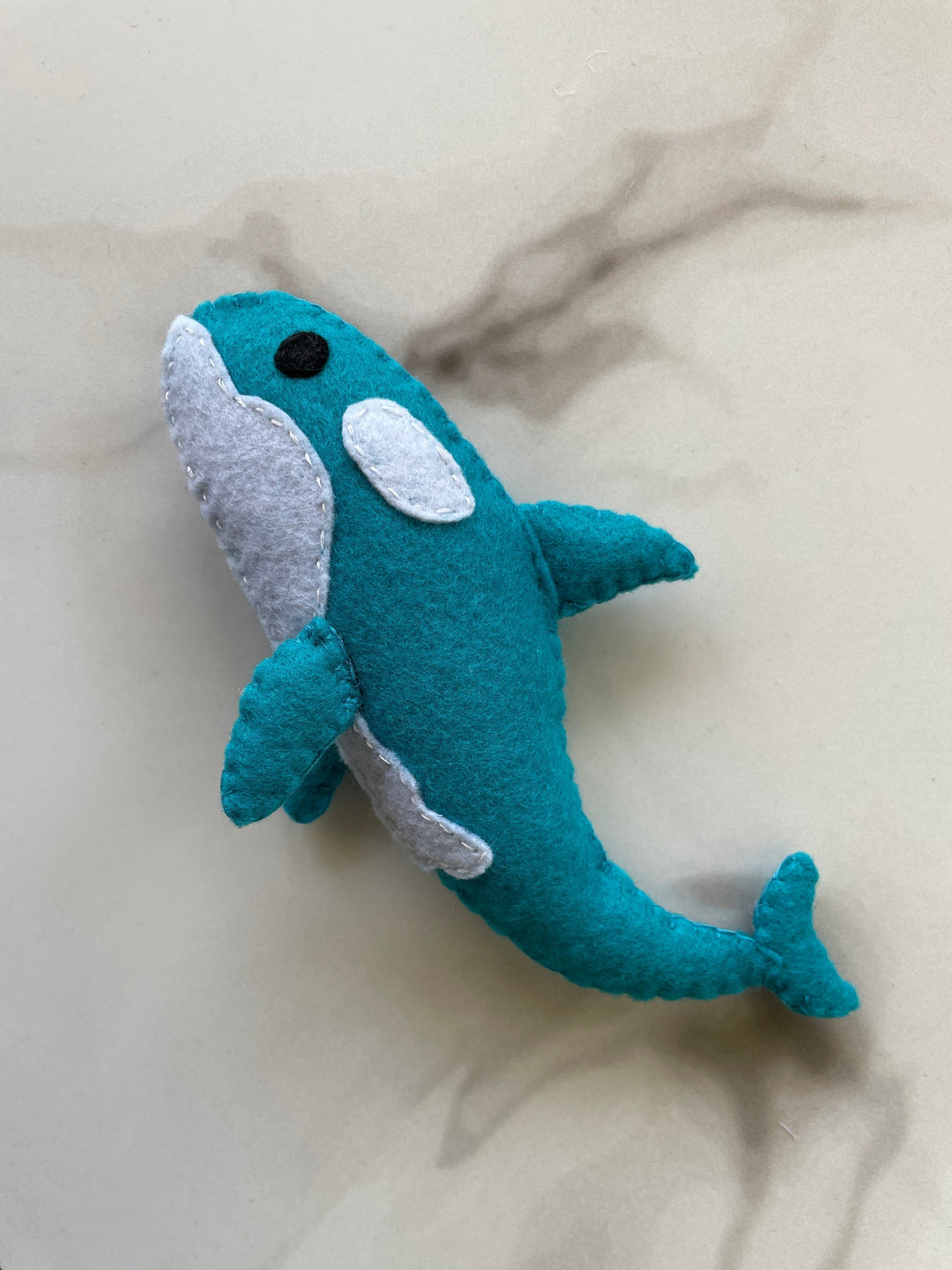 Handmade felt whale plush craft made with blue and white felt fabric, shown on a light marbled background – beginner sewing project from FabricLA DIY kit
