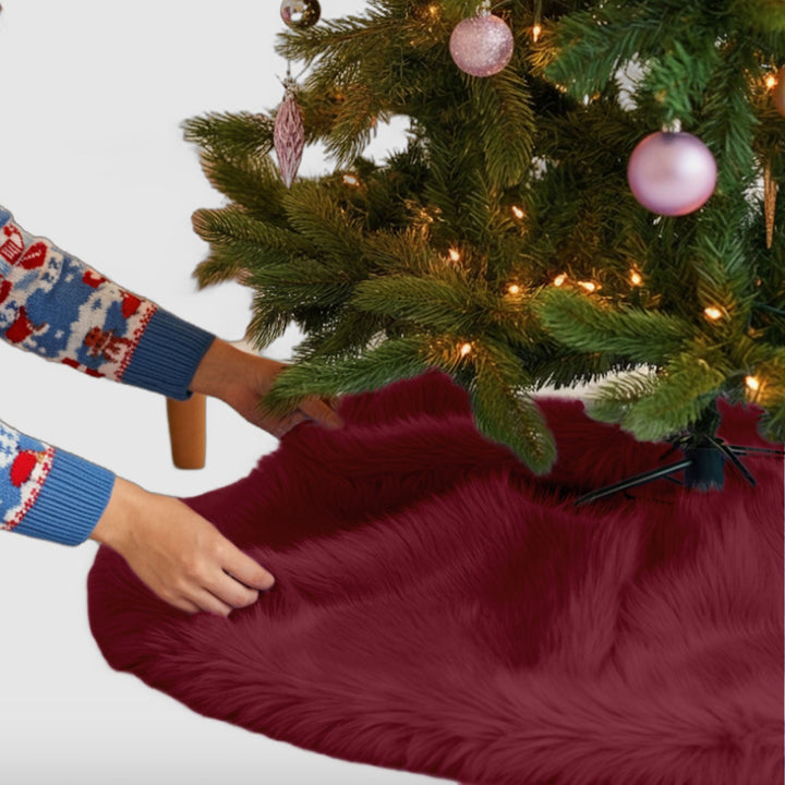 A Burgundy color faux fur Christmas tree skirt placed under a decorated Christmas tree, emphasizing holiday decor.