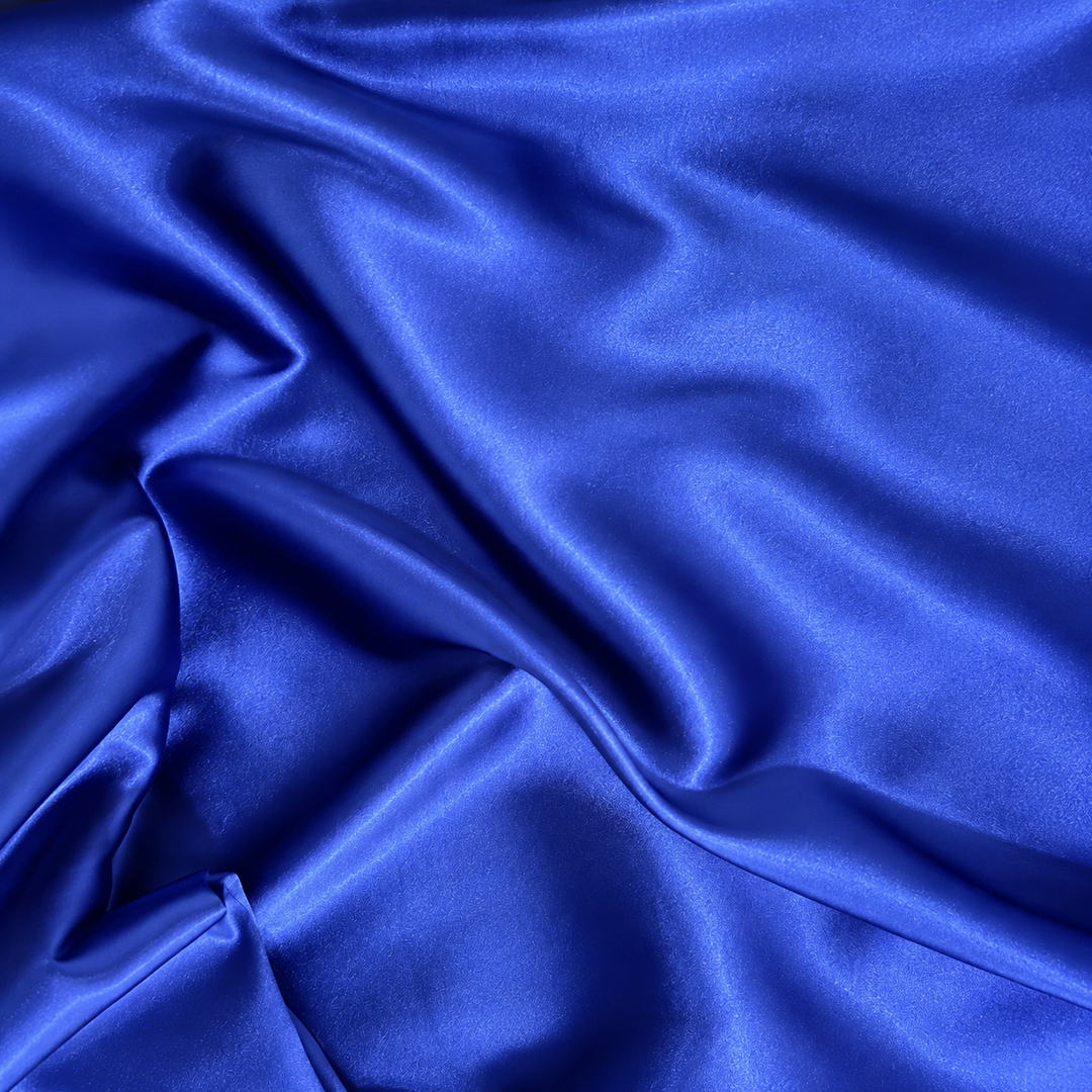 A close-up of draped royal blue satin fabric with soft folds and a glossy sheen.