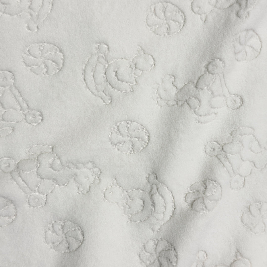 Close-up of embossed rocking horse, teddy bear and pinwheel pattern on ivory fleece