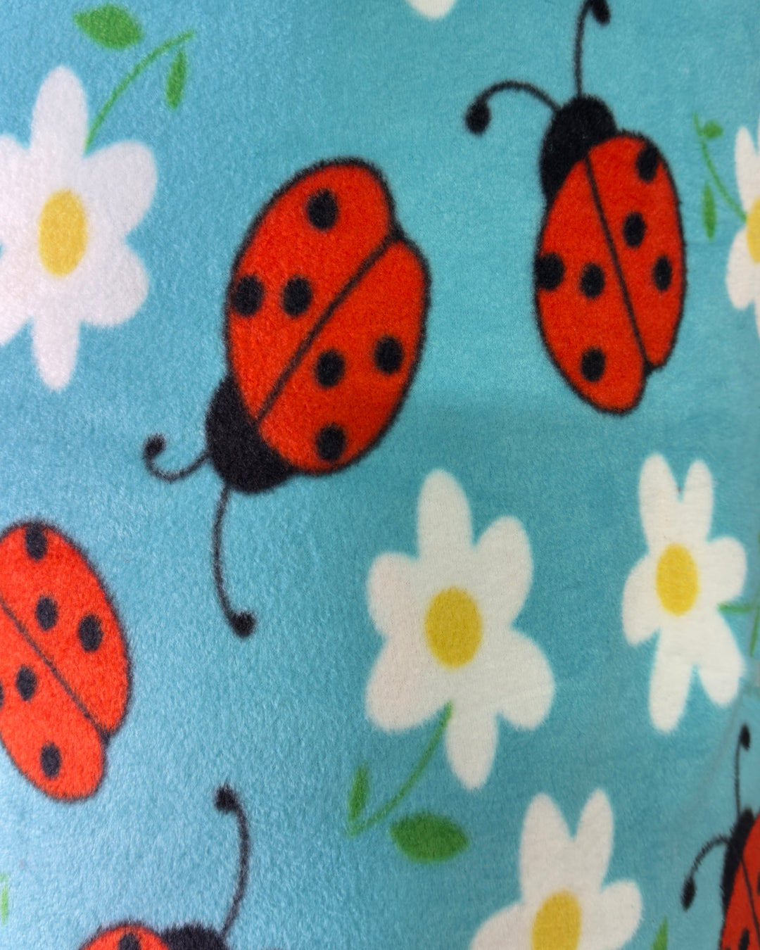 Pattern of red ladybugs and white flowers with yellow centers on a blue background